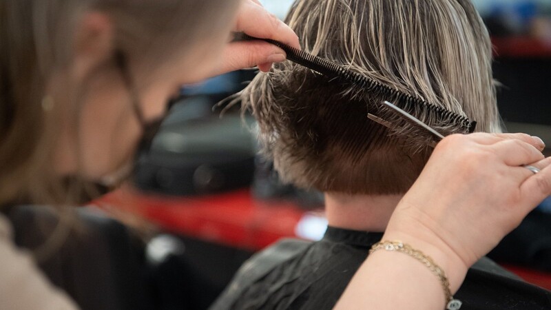 Eine Friseurin schneidet einer Kundin die Haare in einem Friseursalon. Die Branche schlägt Alarm: In Straubing ist die Zahl der Auszubildenden auf einem neuen Tiefststand.