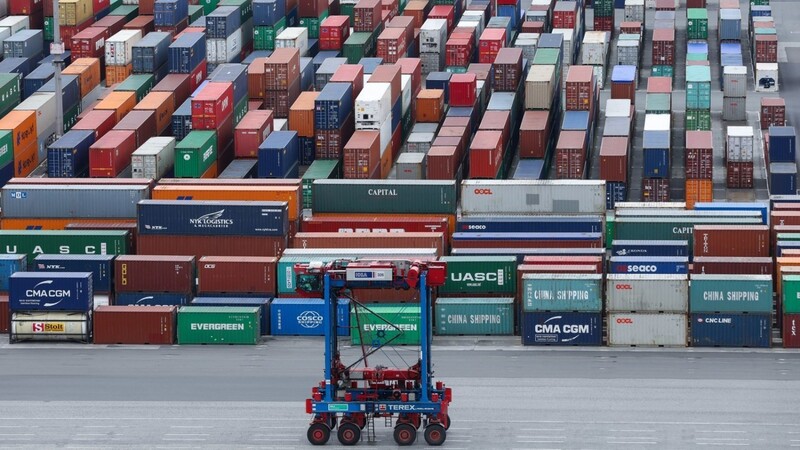 Ein Van-Carrier (VC) fährt über den Container-Lagerplatz am Containerterminal Burchardkai im Hafen an einer Reihe gestapelter Container vorbei. (Symbolbild)