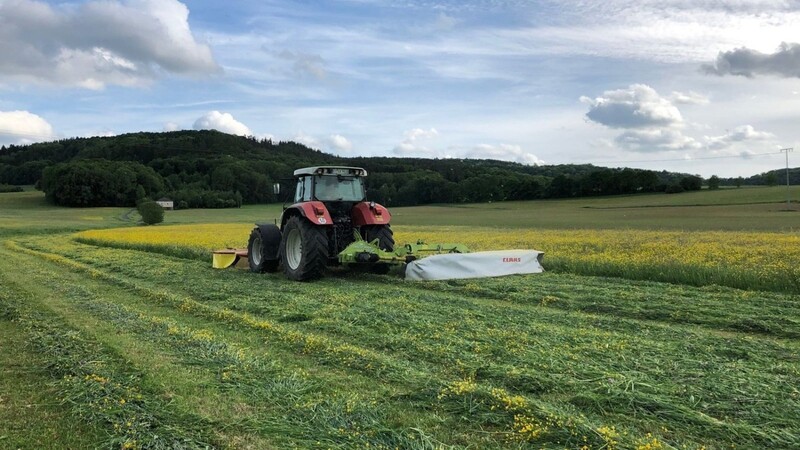 Ein Landwirt mäht im bayerischen Ahorntal mit einem Frontmähwerk und einem Heckmähwerk Gras. Daraus wird Silage zur Viehfütterung.