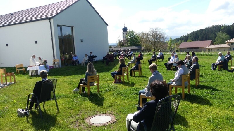 Die Gottesdienstfeier im Pfarrgarten vor dem Max Kolbe-Haus wurde sehr gut angenommen; im Bild Pater John und Diakon Peintinger am Altar und ein Teil der Gläubigen, in Sichtweite der Pfarrkirche St. Bartholomäus.