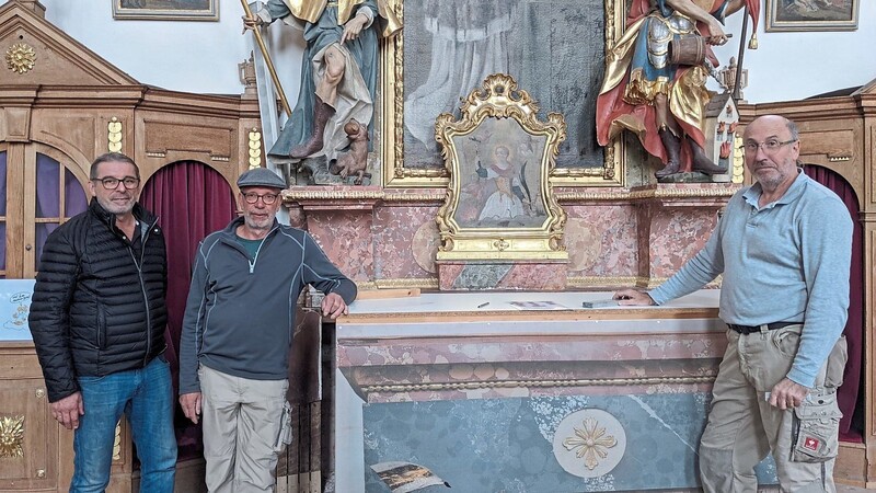 Noch als "Altar-Atrappe" kaschiert: Der nördliche Langhaus-Altar mit den Figuren des Heiligen Rochus (l.) und des Heiligen Florian ist der Muster-Altar für die aufwendige Restaurierung. Dass es nun losgehen konnte, darüber freuen sich (v.l.) Kirchenpfleger Georg Obermaier sowie die Stuckrestauratoren Christian Wegerhoff und Thomas Salveter.