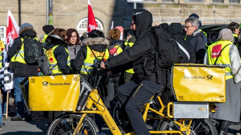 Ein Postbote radelt in Bielefeld an Streikenden einer Verdi-Aktion vorbei.