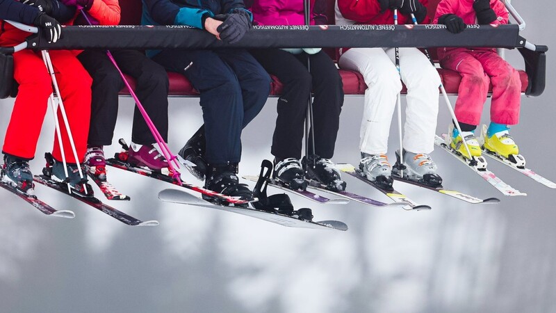 Skifahrer im Sessellift. Das schöne Bergpanorama hat man bei der Fahrt auf den Berg leider immer nur im Rücken.