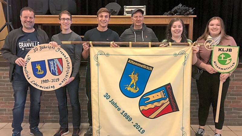 Präsentation der Gastgeschenke Taferl, Freundschaftsfahne und Schützenscheibe durch (v. r.) die KLJB-Vorsitzenden Sophia Müller und Karolina Zellmeier, Ratsmitglied Tom Borgelt, KLJB-Vorsitzenden Bastian Glöbl sowie die beiden Schützenvorstände Rainer Dicke und Stefan Zellmeier.