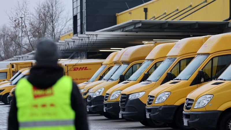 Am Zustellstützpunkt der Deutschen Post DHL am Hauptbahnhof in Rostock haben sich Mitarbeiter zum Warnstreik eingefunden, im Hintergrund stehen die Zustellfahrzeuge.