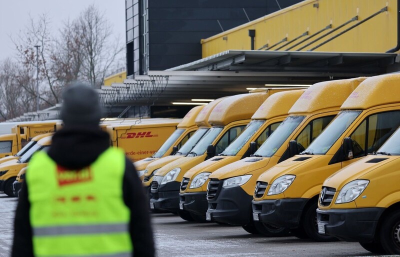 Am Zustellstützpunkt der Deutschen Post DHL am Hauptbahnhof in Rostock haben sich Mitarbeiter zum Warnstreik eingefunden, im Hintergrund stehen die Zustellfahrzeuge. 