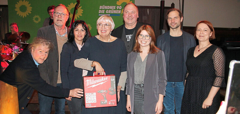 Grünen-Bezirksrat Markus Scheuermann (v.l.), Bezirkstags-Kandidat Kay Hoppe, Landtagskandidatin Feride Niedermeier, Ministerin Claudia Roth mit Bohrmaschine zum Bohren dicker Bretter, MdB Erhard Grundl, MdB Marlene Schönberger, MdL Toni Schuberl und Bezirksrätin Mia Goller. Im Hintergrund Michael "Eumel" Aumer mit Band. 