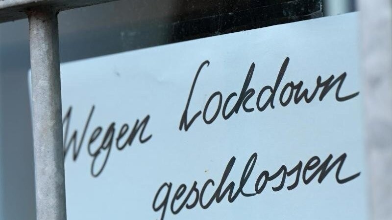 Ein Zettel mit der Aufschrift "Wegen Corona geschlossen" hängt am Schaufenster eines Geschäfts.