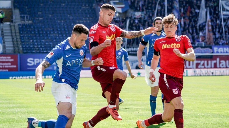 Rostocks Ryan Malone (v.l.), Regensburgs Erik Wekesser und David Otto kämpfen in einem hart umkämpften Spiel um den Ball.