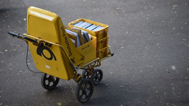 Ein Trolley eines Zustellers der Deutschen Post steht auf der Straße.