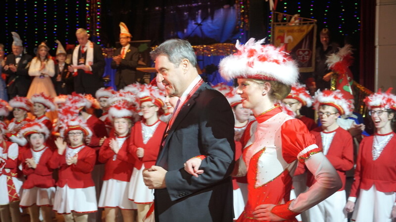 Ministerpräsident Markus Söder geleitet von einem Gardemädchen.