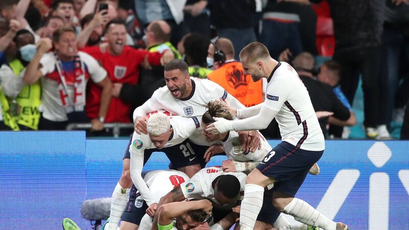 Harry Kane (unten) schießt England ins EM-Finale und wird dafür von seinen Teamkollegen fast erdrückt. Die Fans auf den Tribünen sind außer Rand und Band.