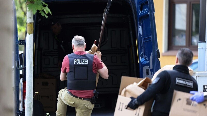 Polizisten tragen Gegenstände, darunter mehrere Stichwaffen und Speere, aus dem Wohnhaus des Verdächtigen.