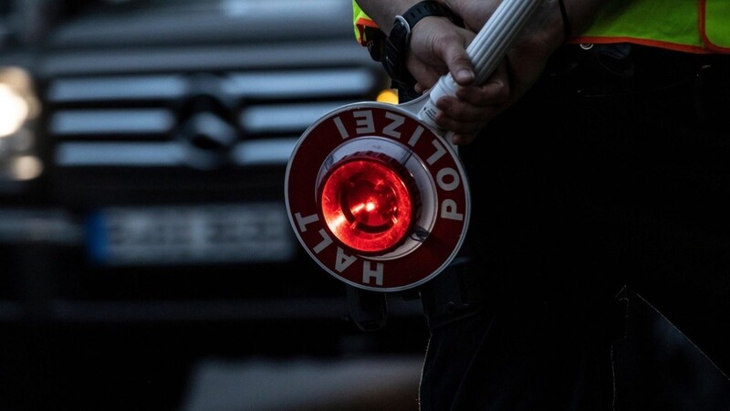 Ein Polizist hält bei einer Verkehrskontrolle eine Winkerkelle in der Hand.